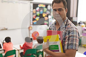 Schoolteacher standingin classroom with book and looking at the camera at school