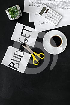 Sciccors and paper with word budget, coffee and plan for budget reducing on black background top view mock-up