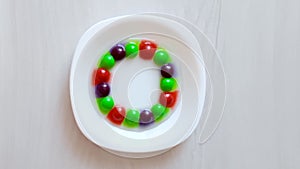 Science experiment for kids. Circle of colored candies on white plate