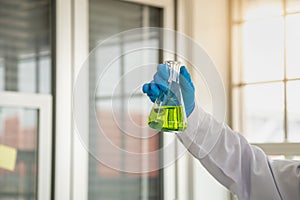 Science and Healthcare Concept. Closeup of docter scientists hand holding green liquid chemicals flask in a laboratory