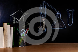 Science Lab set up and Square Academic cap drawn by colored chalk with books, pen stand, and Stationary items placed on a table