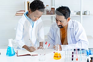 Science teacher teaches a male student of African descent to take notes on a science experiment. derived from learning to lead to