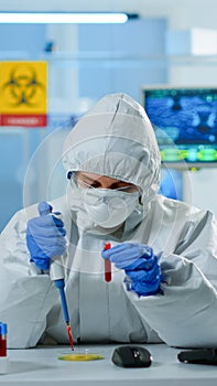 Science technician in ppe suit using micropipette and petri dish analysing blood sample