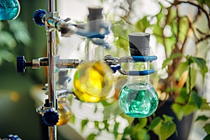 Scientific glass flasks containing green and yellow chemical reagent liquid holding by clamp for students or researchers.