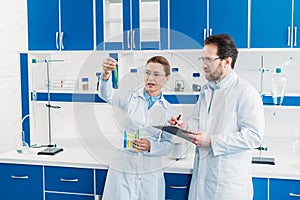 scientific researchers in white coats and eyeglasses with flasks and notepad