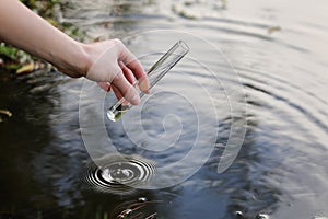 Scientist and biologist hydro-biologist takes water samples for analysis outdoors. Hand is collects water in a test tube. Pond