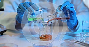 Scientist carefully mixing green and red liquids in glass beaker