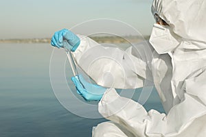 Scientist in chemical protective suit with test tube taking sample from river for analysis