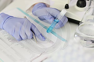 Scientist chemist checking composition of liquid in test tube in accordance with norms in table closeup