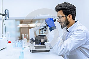 Scientist conducts experiments, adjusts specimen in petri dish and looking on it into microscope