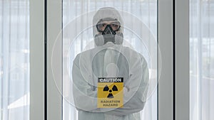 Scientist with coverall protection clothing and full face protection mask in control room with radiation hazard sign