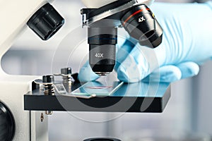 Scientist examining sample of red liquid on slide under microscope in laboratory, closeup