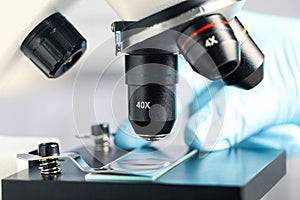 Scientist examining sample of red liquid on slide under microscope in laboratory, closeup