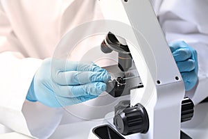 Scientist examining sample on slide under microscope at table, closeup