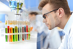 Scientist in eyeglasses looking at test tubes with reagents in lab