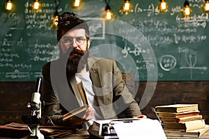 Scientist in glasses type on vintage typewriter. Scientist with beard typewrite research paper with microscope and books