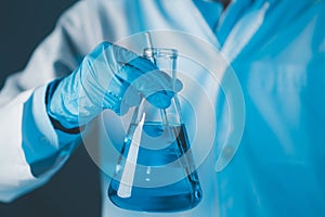 Scientist hand hold erlenmeyer flask with stirring rod filled with blue sample chemicals in chemistry science laboratory.