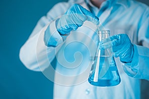 Scientist hand hold erlenmeyer flask with stirring rod filled with blue sample chemicals in chemistry science laboratory.