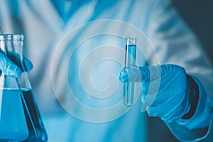 Scientist hand hold test tubes and erlenmeyer flask filled with blue sample chemicals in chemistry science laboratory. Glassware