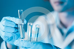 Scientist hand hold test tubes filled with blue sample chemicals in chemistry science laboratory. Glassware in medical research.