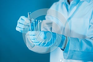 Scientist hand hold test tubes filled with blue sample chemicals in chemistry science laboratory. Glassware in medical research.