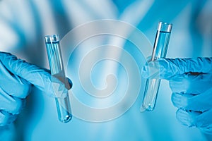 Scientist hand hold test tubes filled with blue sample chemicals in chemistry science laboratory. Glassware in medical research.