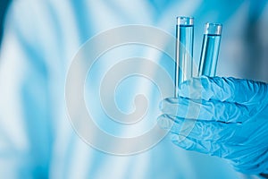 Scientist hand hold test tubes filled with blue sample chemicals in chemistry science laboratory. Glassware in medical research.