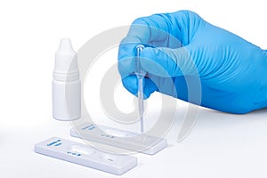 Scientist hand wearing blue surgical gloves, placing the sample into the covid-19 antigen diagnostic test device, on white