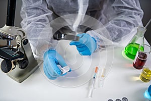 Scientist in hazmat suit and goggles holding vaccine bottle and magnifying glass, looking and research. Epidemiology virus test.