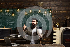 Scientist hipster with lightbulb on chalkboard. Bearded man hold bulb in classroom. Businessman in suit at school desk