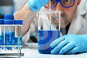 Scientist holding beaker with blue liquid for analysis of fluids in the lab