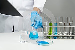 The scientist holding the clipboard and blue liquid flask