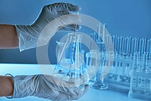 Scientist holding conical flask with liquid and pipette in laboratory