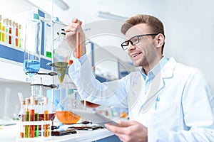 Scientist holding digital tablet and looking at test tube in lab