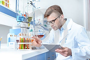 Scientist holding digital tablet and working with test tubes in lab