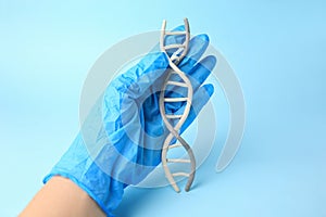Scientist holding DNA molecule model made of colorful plasticine on light blue background, closeup