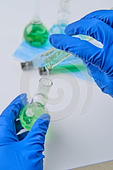 Scientist holding flask and tube at laboratory, closeup. Solution chemistry. Antivirus solution. Blue and green liquid