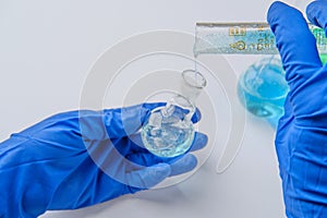 Scientist holding flask and tube at laboratory, closeup. Solution chemistry. Antivirus solution. Blue and green liquid