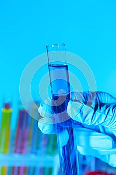 Scientist holding test tube with liquid on light blue background, closeup