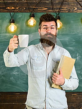 Scientist holds book and drinks coffee, chalkboard on background, copy space. Coffee break concept. Man with beard on