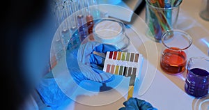 Scientist holds a litmus paper strip next to beakers of colored liquids to test pH levels