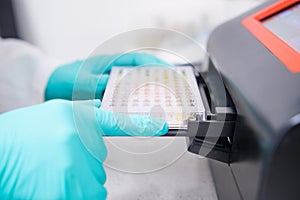 A scientist inserts a microplate into a microplate spectrophotometer for biological analysis.