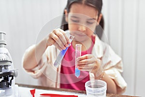 The scientist kid testing chemistry lab experiment with a microscope in the school. Little girl looking at two flasks containing