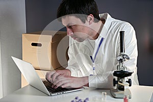 Scientist in lab coat and eyeglasses working at workplace with laptop in laboratory. Male doctor researcher are doing