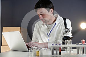 Scientist in lab coat and eyeglasses working at workplace with laptop in laboratory. Male doctor researcher are doing