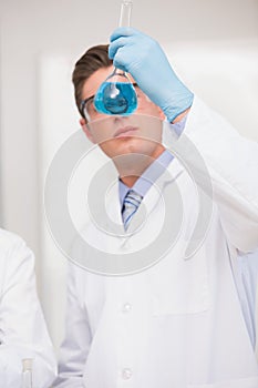 Scientist looking at beaker with blue fluid