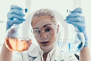 Scientist looks at Liquid Samples in Flasks in Lab