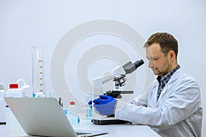 Scientist man doing chemical experiment, making analyzing, looking sample under microscope