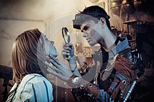 A scientist, a mechanic, examines in a magnifying glass an artificial robot girl in his steampunk lab.
