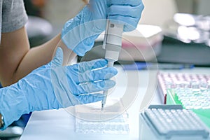 Scientist pipette dropping a sample into a test microtiter plate